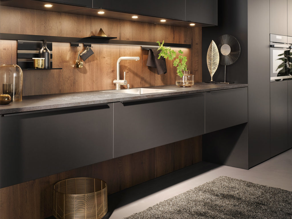 Cocina moderna con mueble suspendido en negro y tirador integrado y frontal de madera con luz led decorativa.